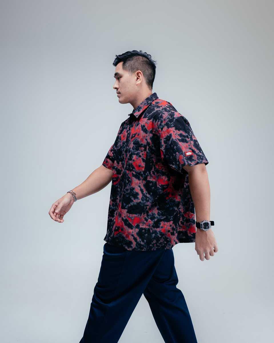 Kemeja Hawaii tie-dye dari koleksi Beach Getaway Vans x TDC, dengan warna hijau-merah dan nuansa musim panas yang santai.